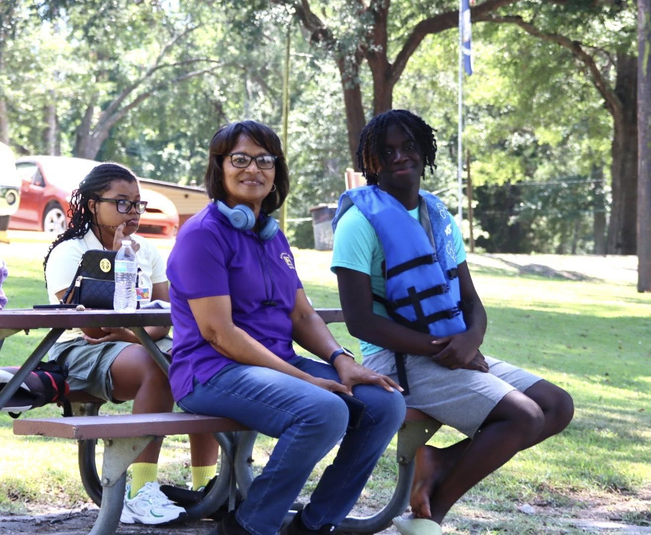 A woman and two teenagers sitting at a picnic table.
